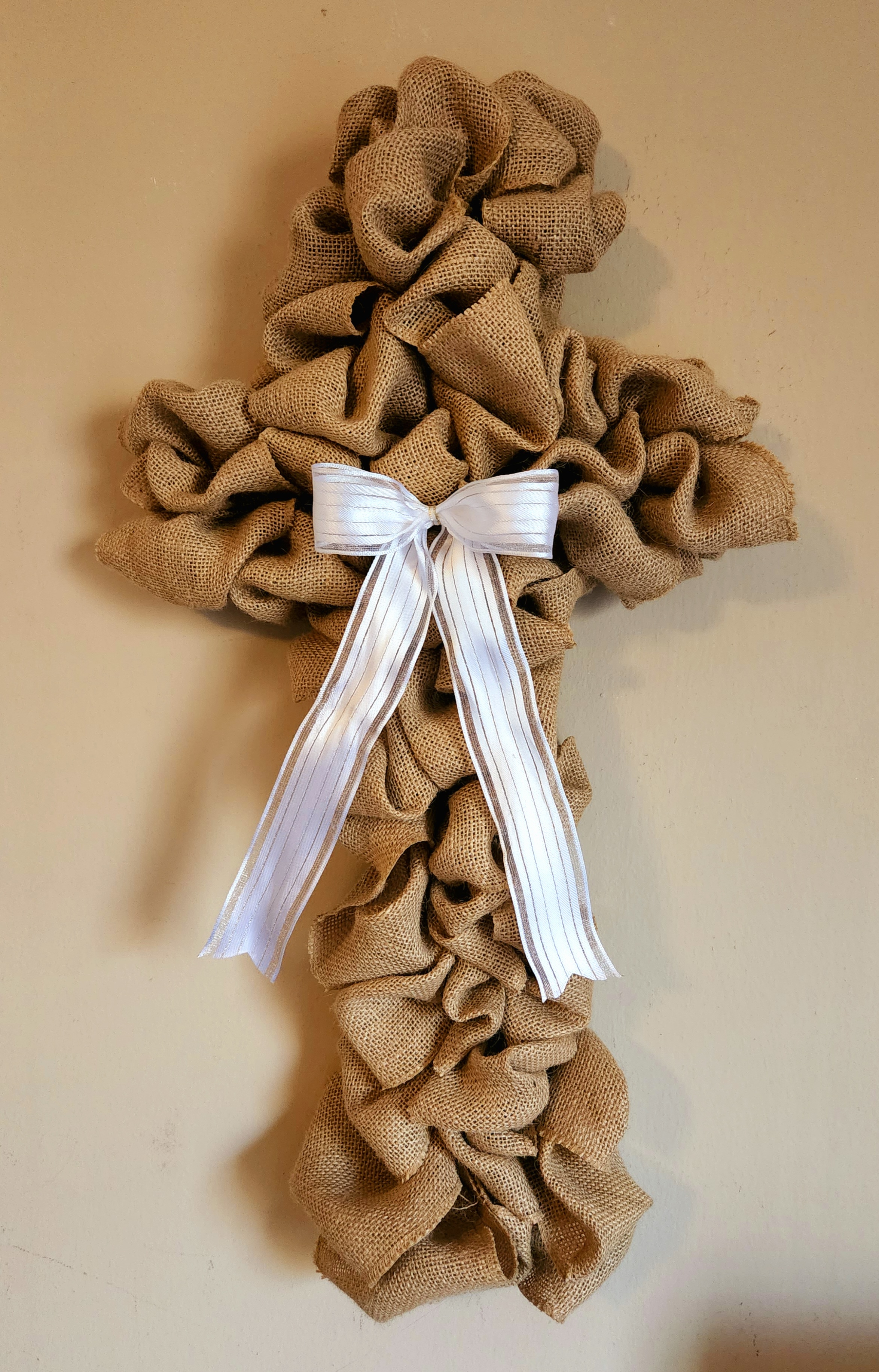 Burlap cross wreath with a white bow in the center of it.
