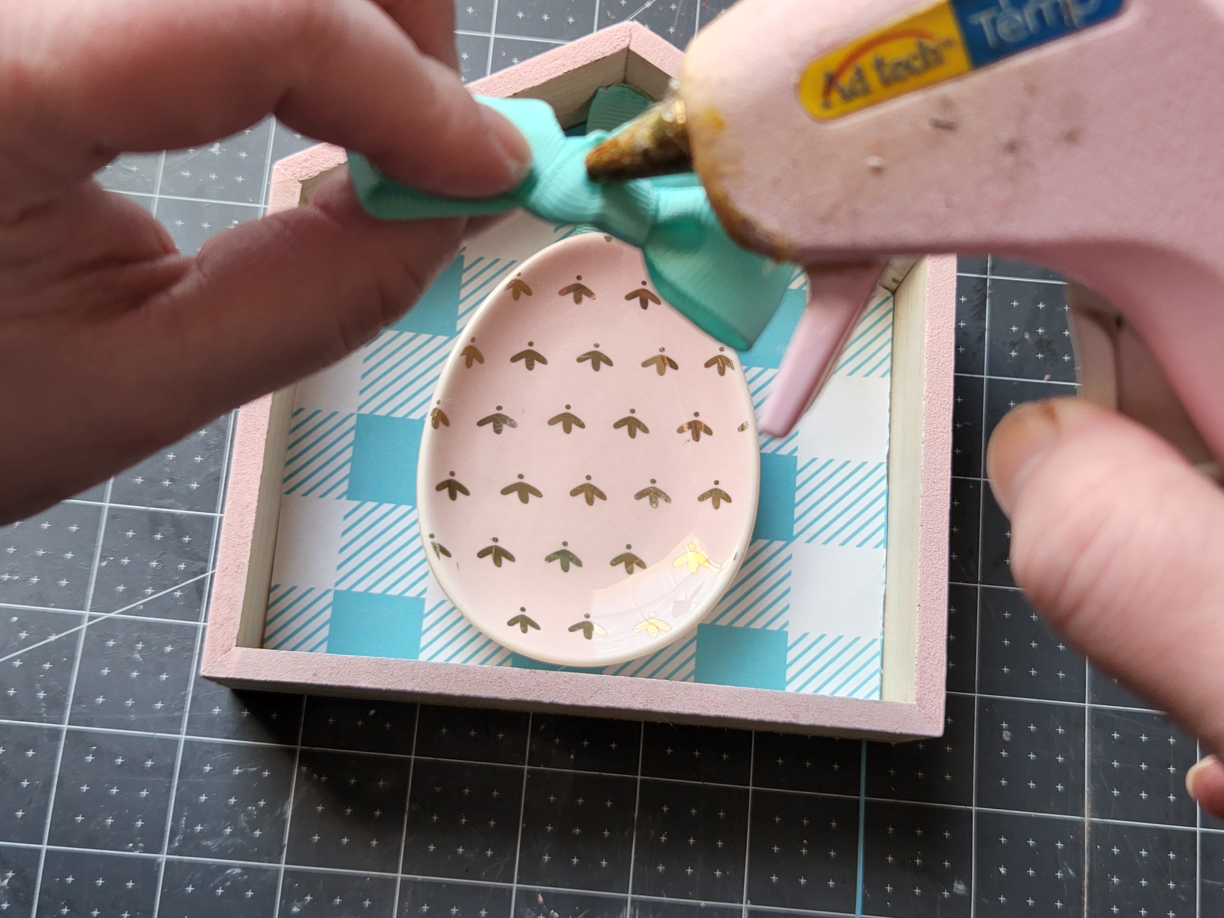 Placing hot glue on the back of an aqua bow to put inside the spring Dollar Tree houses.