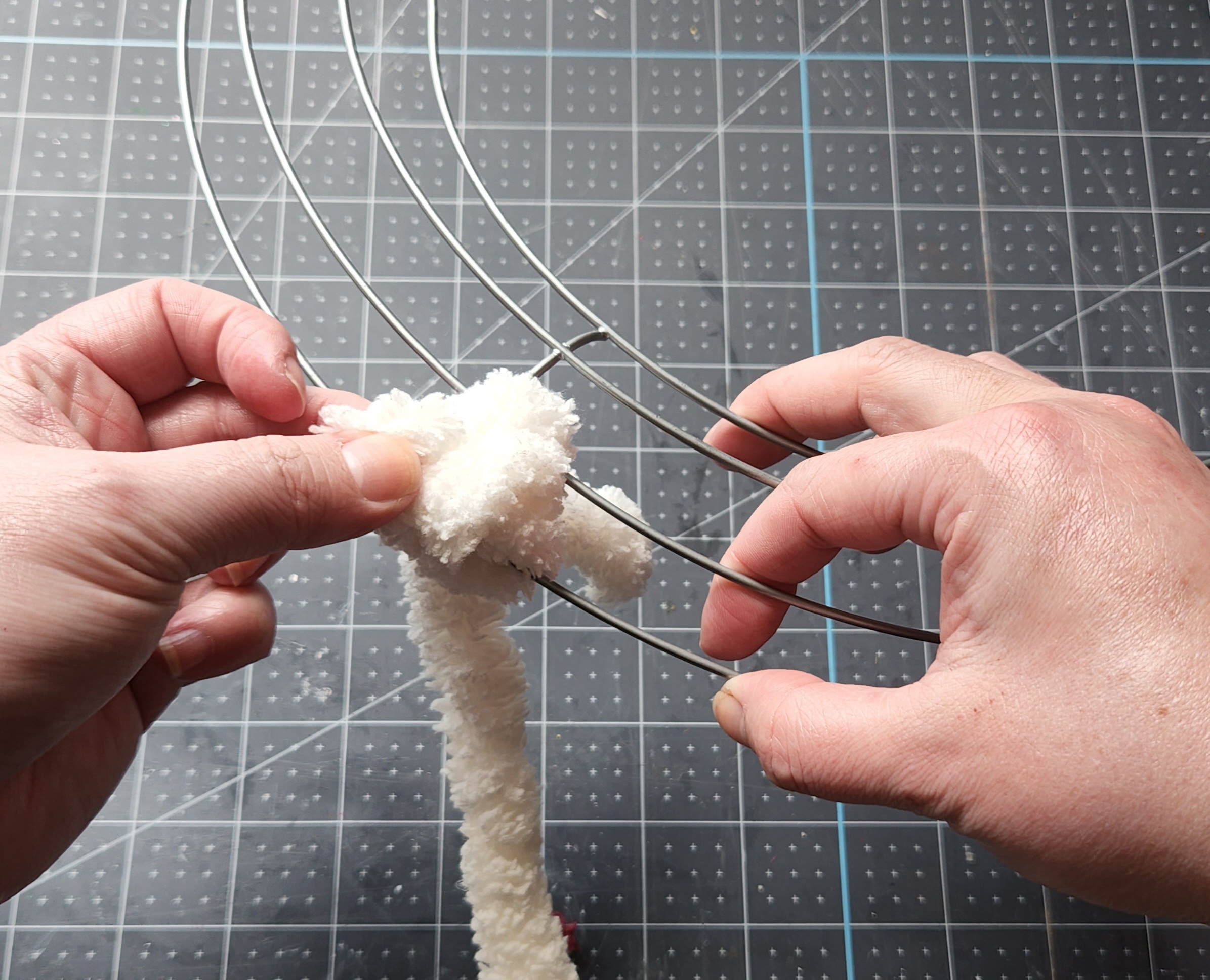 Tying a slip knot around the outer two rings of the wreath form with the cream yarn.