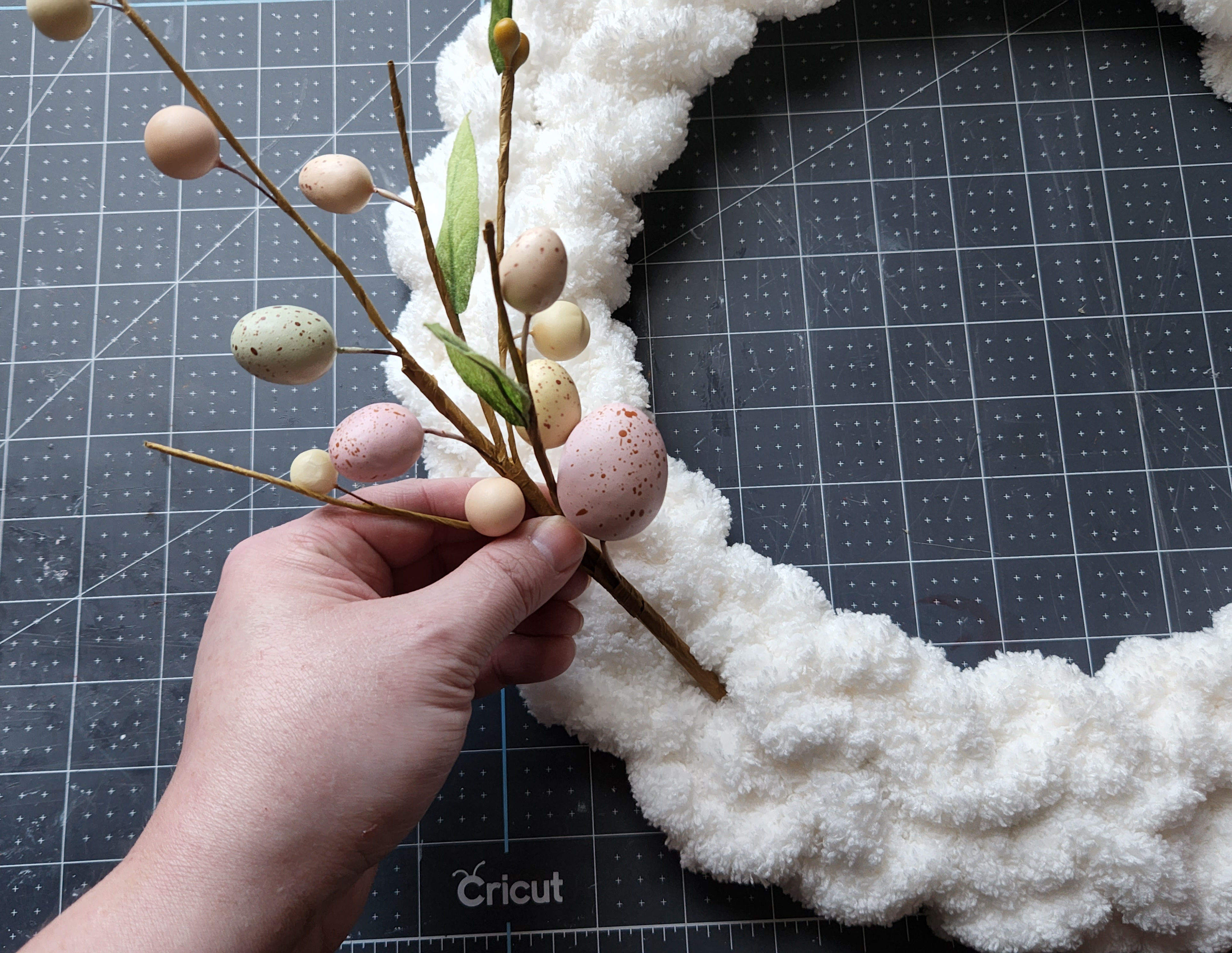 Placing a speckled egg pick into the braided chunky yarn wreath.