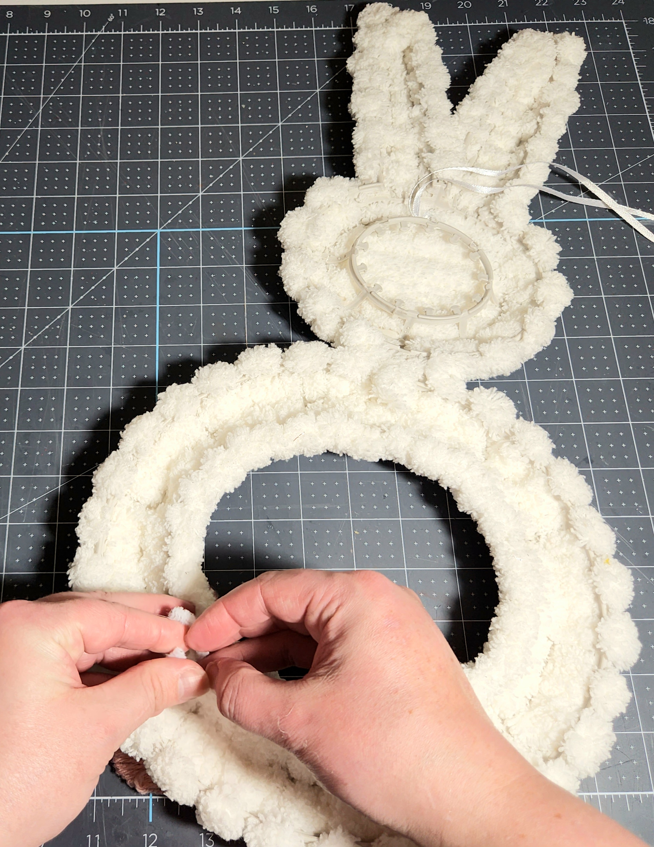 Placing the pink yarn-covered bunny paws through the front of the wreath with wire & twisting it closed in the back.