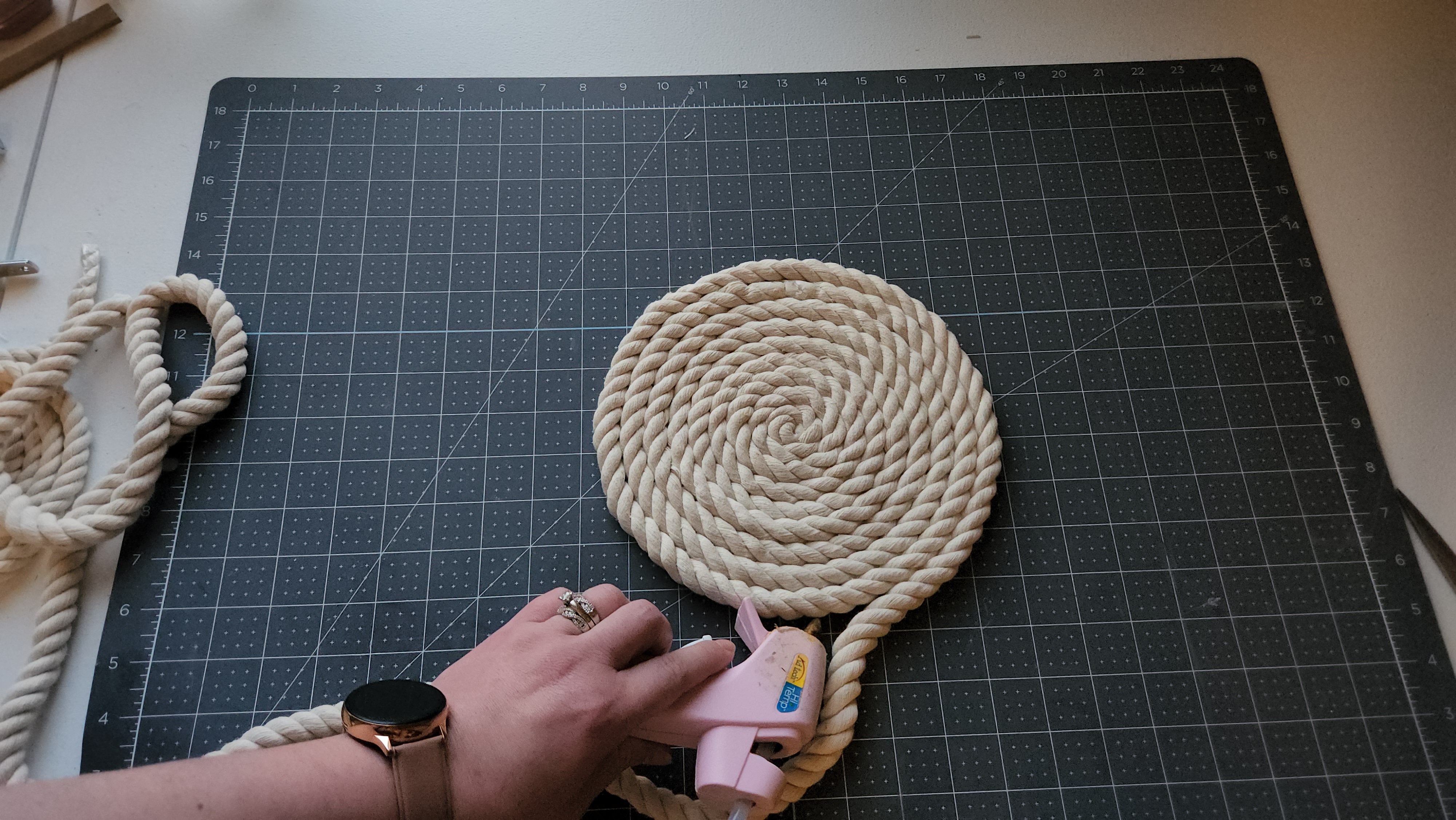 Adding hot glue to the edge of the cotton rope that's forming the rope placemat to roll the rest of the rope on it.