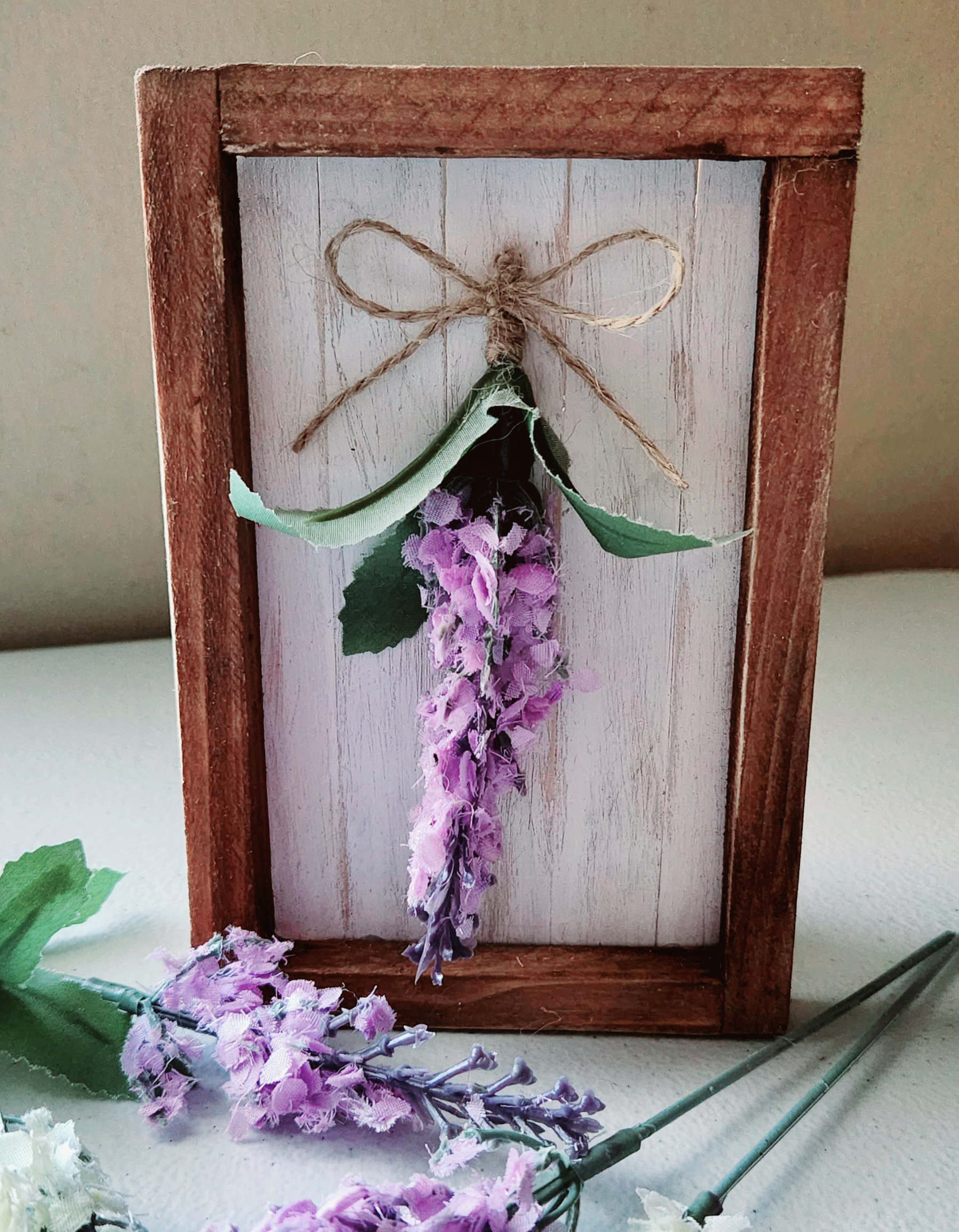 Dollar Tree canvas DIY shiplap project: white shiplap looking popsicle sticks glued inside the wood frame of a Dollar Tree canvas with a lavender flower and twine bow glued in the center.