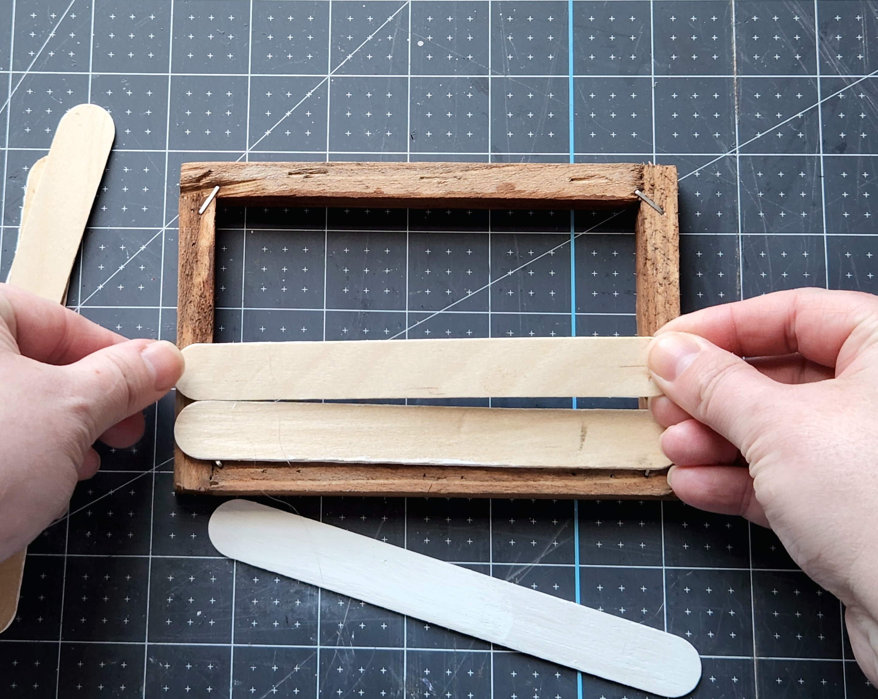 Placing a painted popsicle stick on top of the hot glue on the back of the wood frame completely covering the opening of the Dollar Tree canvase frame.