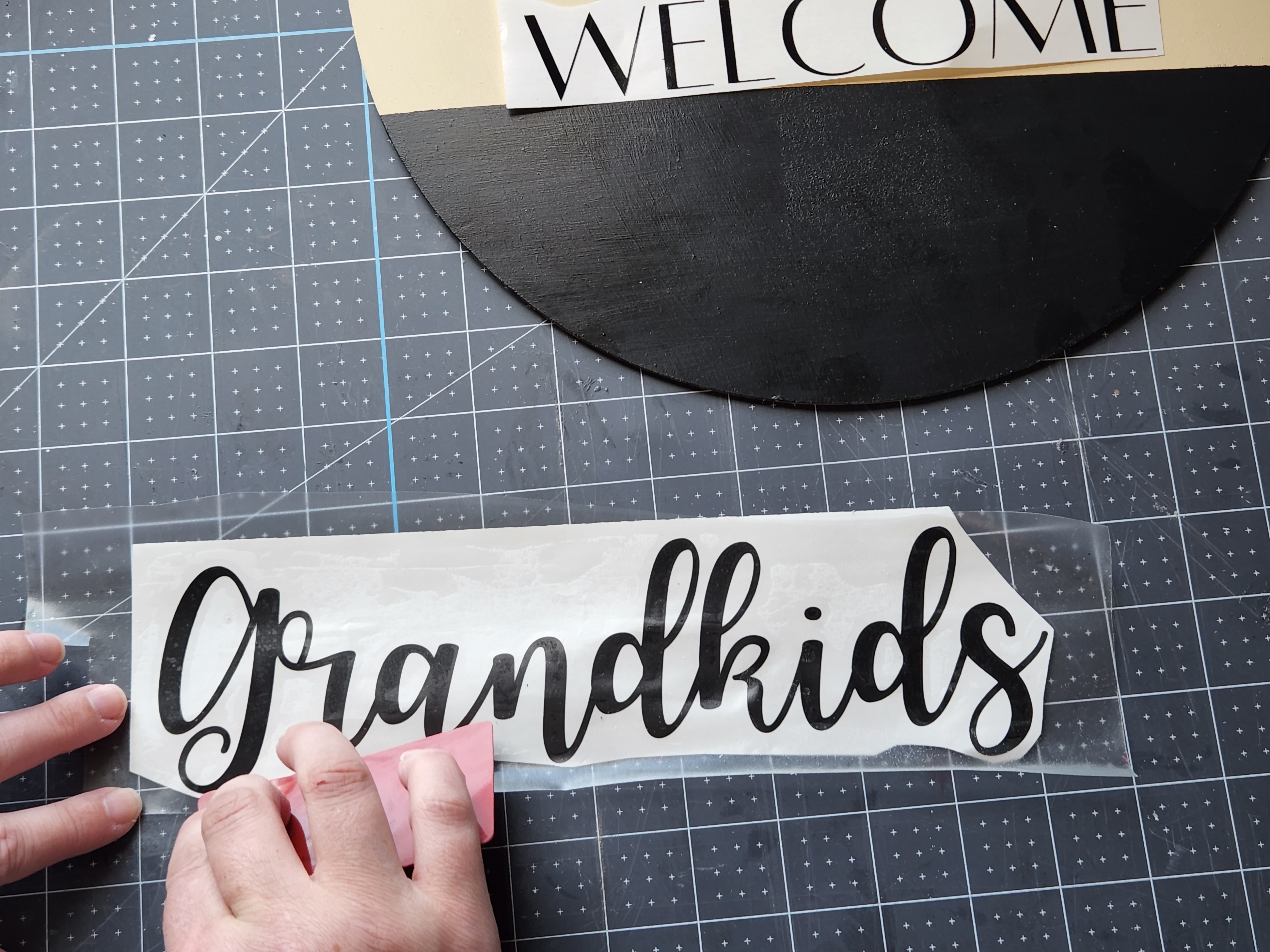 Smoothing transfer tape onto "grandkids" vinyl design with a credit card.