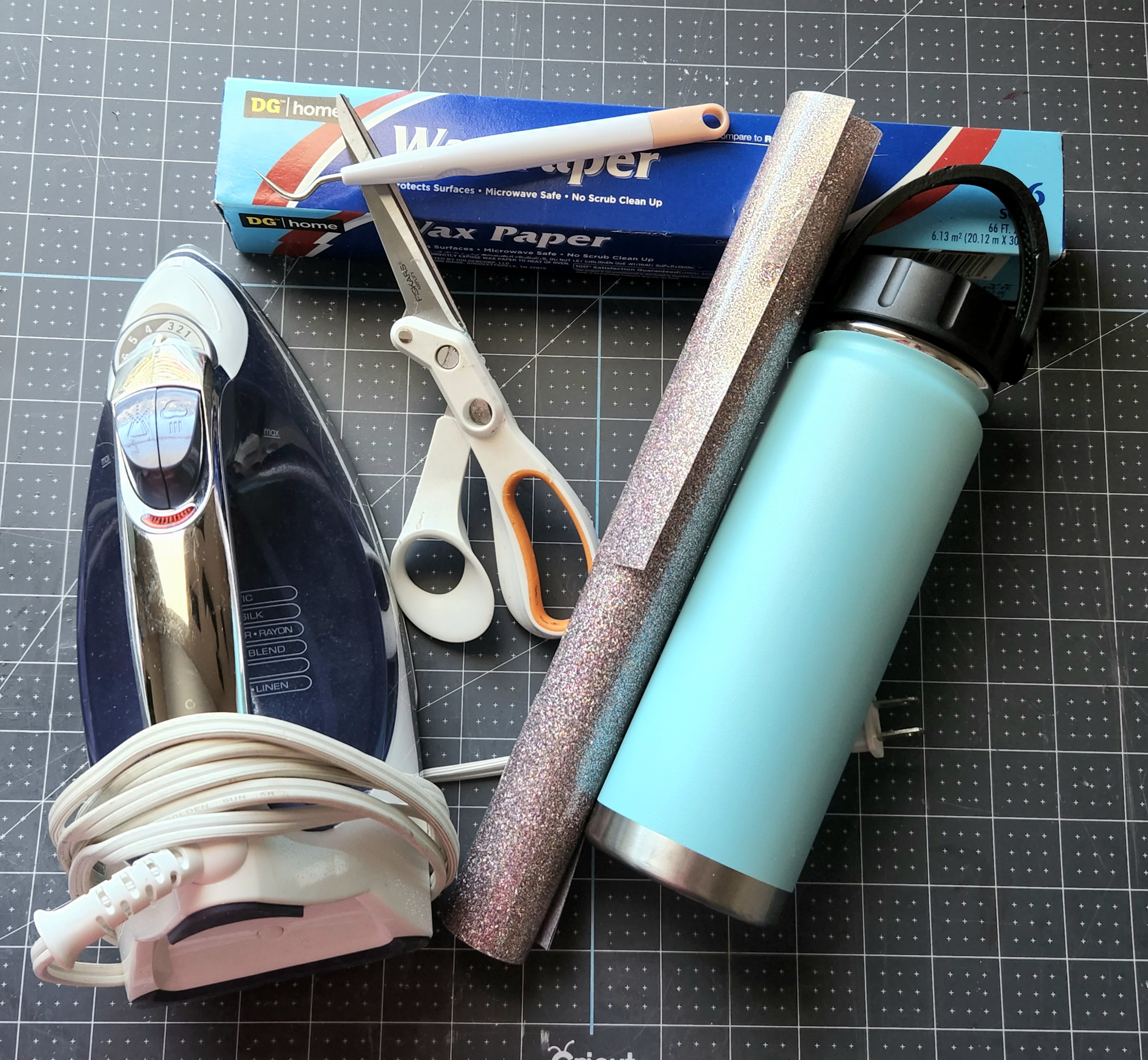 Supplies to cut a child's handwriting with a Cricut for a DIY gift: iron, wax paper, weeding tool, scissors, unicorn glitter colored HTV, and an aqua tumbler.