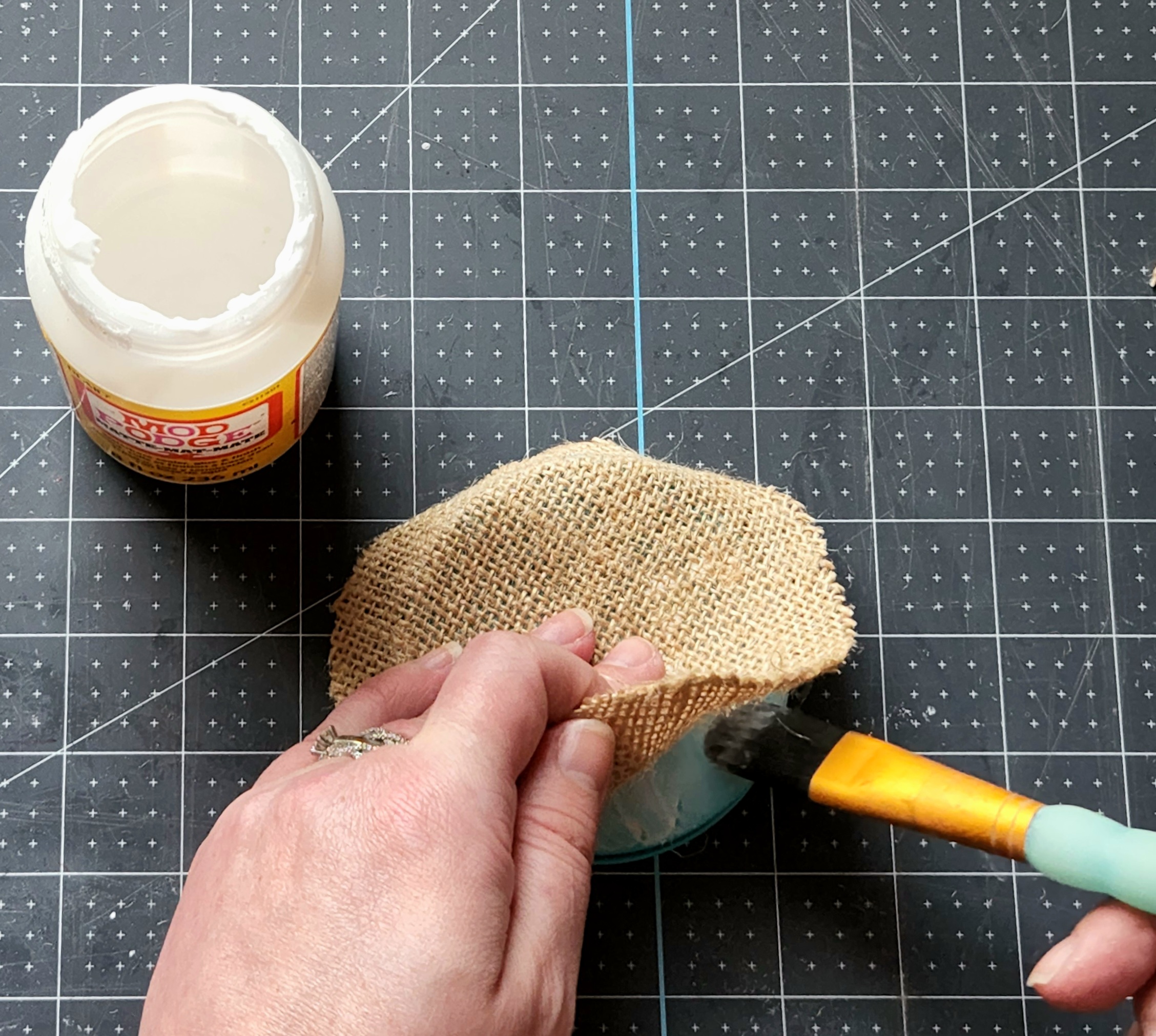 Painting Mod Podge under the burlap on the jar lid before smoothing it out.