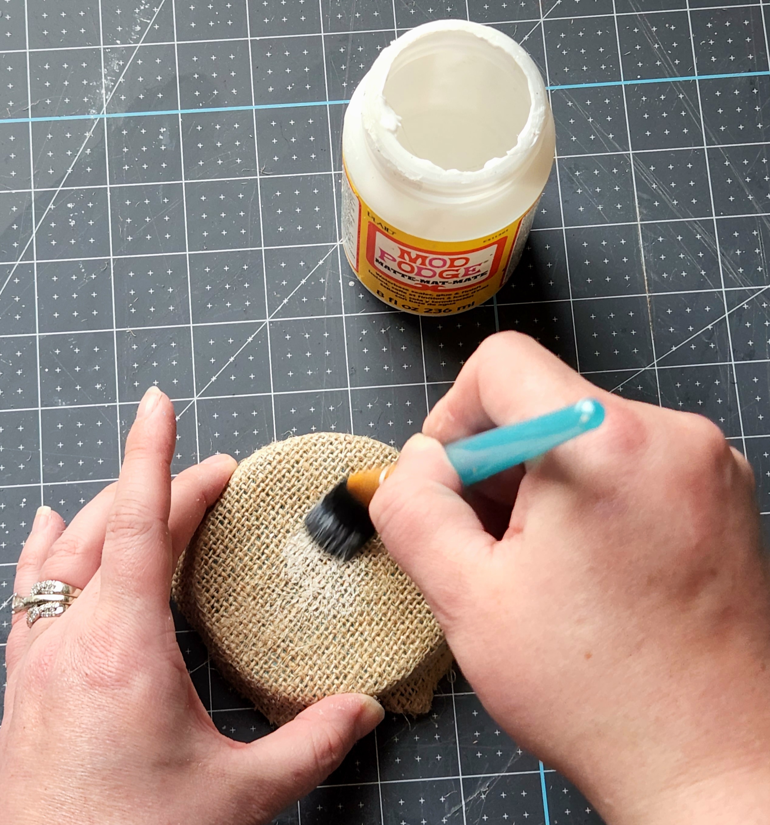 Adding Mod Podge to the top of the jar lid covered in burlap.