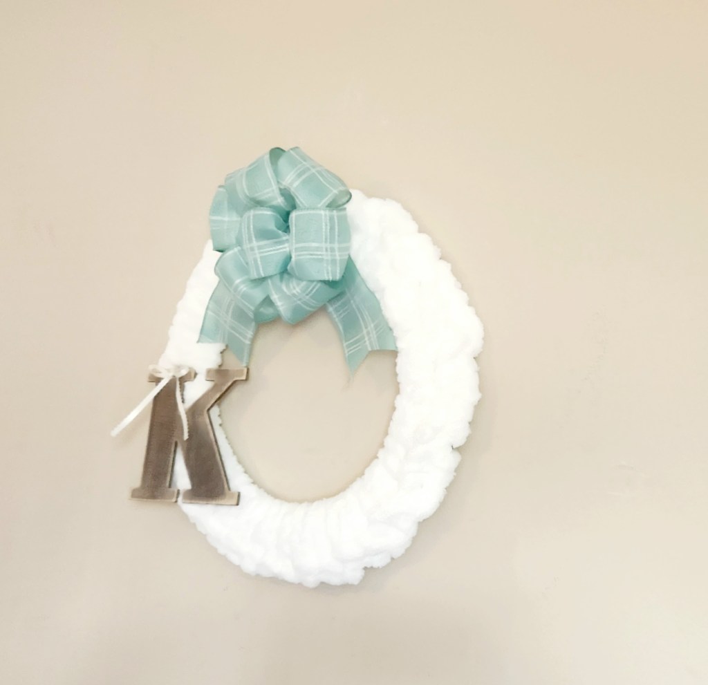 Hand crocheted chunky yarn wreath: Completed hand crocheted chunky yarn wreath made with cream yarn & embellished with a sage and ivory 7 loop bow in the top center and an aged wood letter K on the bottom left side attached with a 1/4" ivory ribbon tied in a bow.