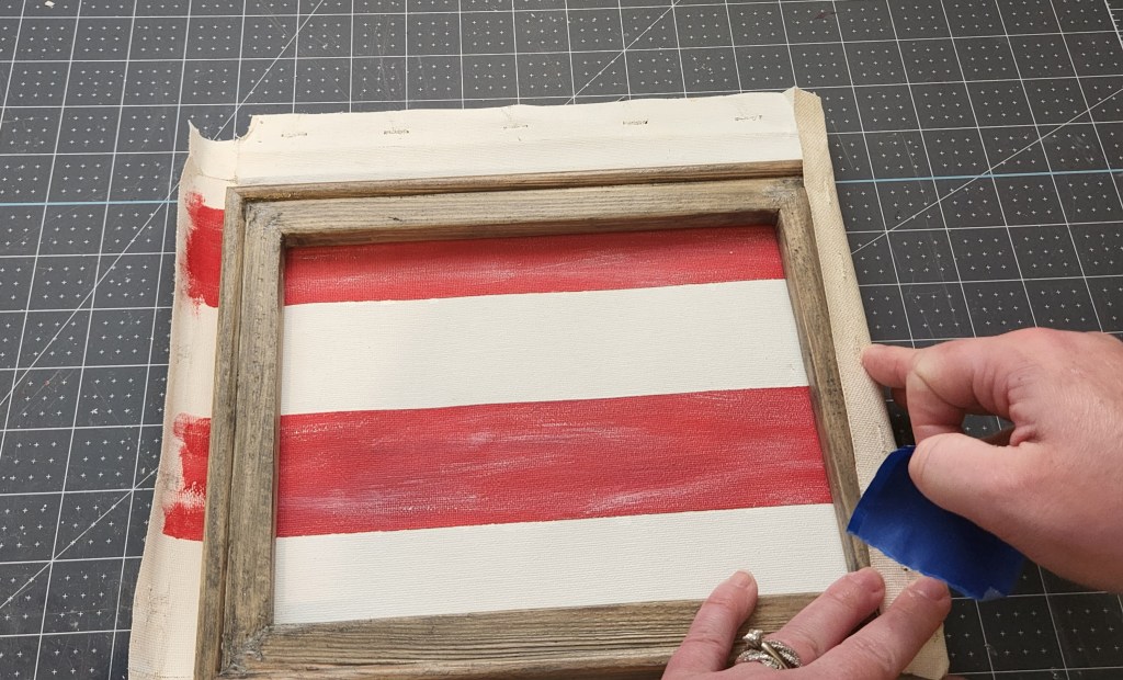 Taping the right side of the canvas around the side of the wood frame of the farmhouse flag.