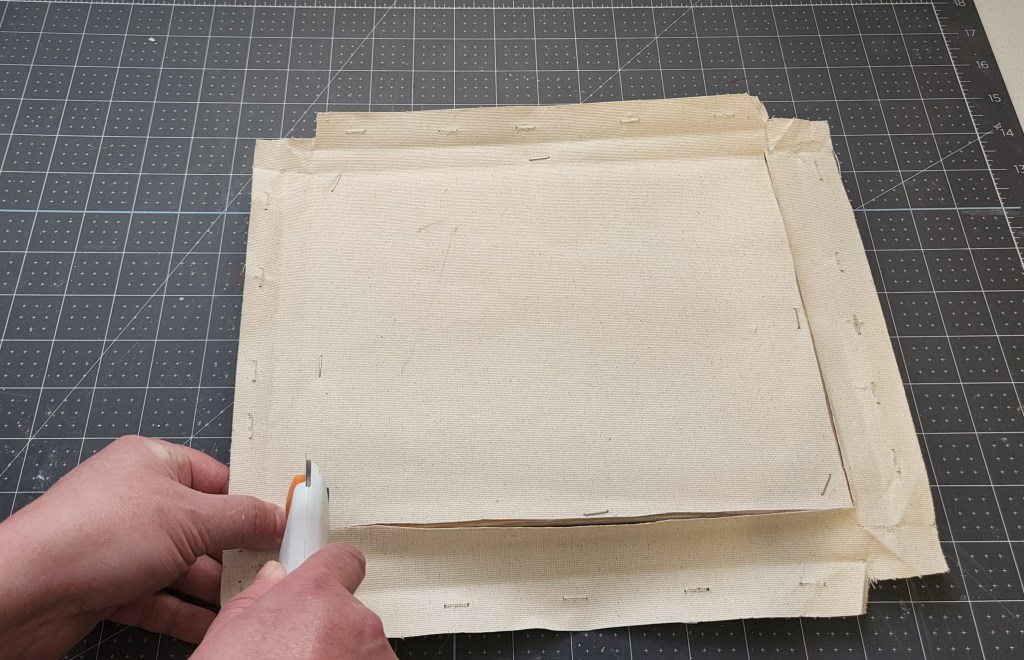 Using a rotary cutter to cut excess canvas off the back of the farmhouse flag's frames.