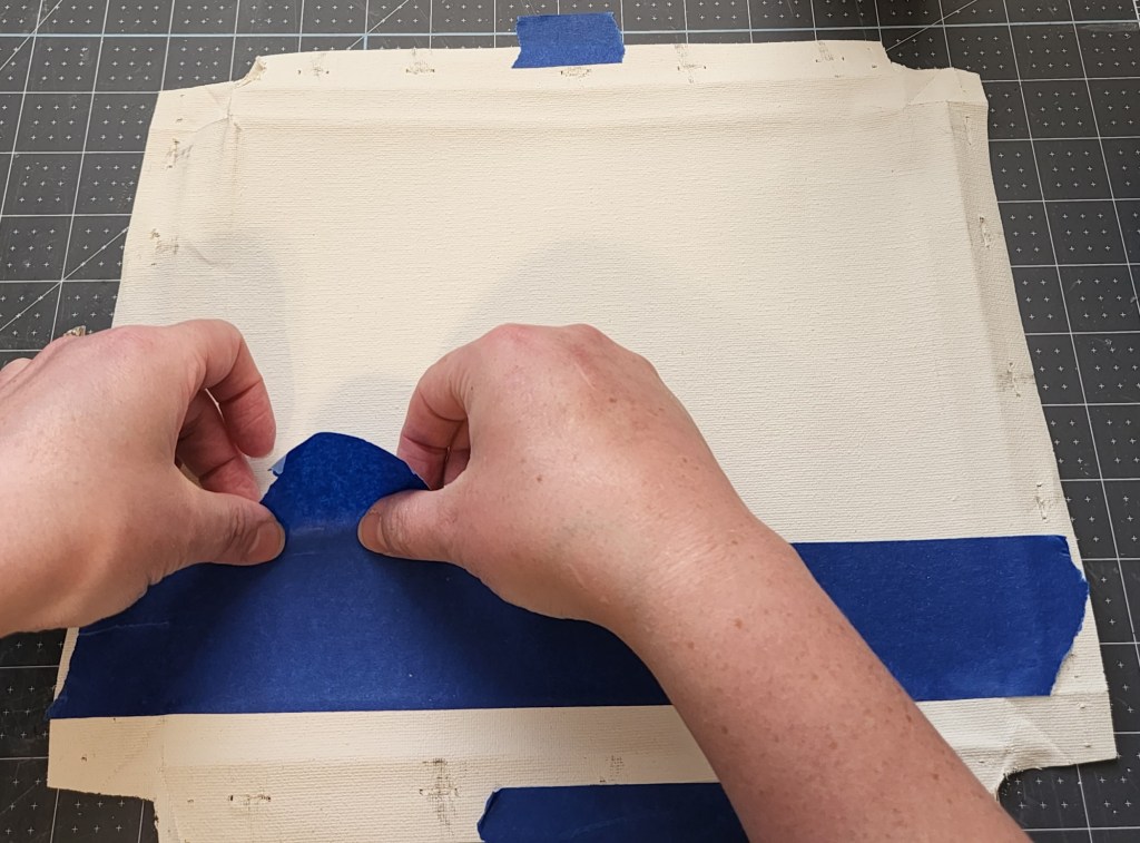 Placing painter's tape alone the first stripe on the canvas.