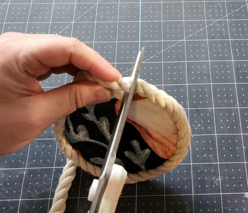 Cutting white cotton rope after gluing it around the edge of the coaster.