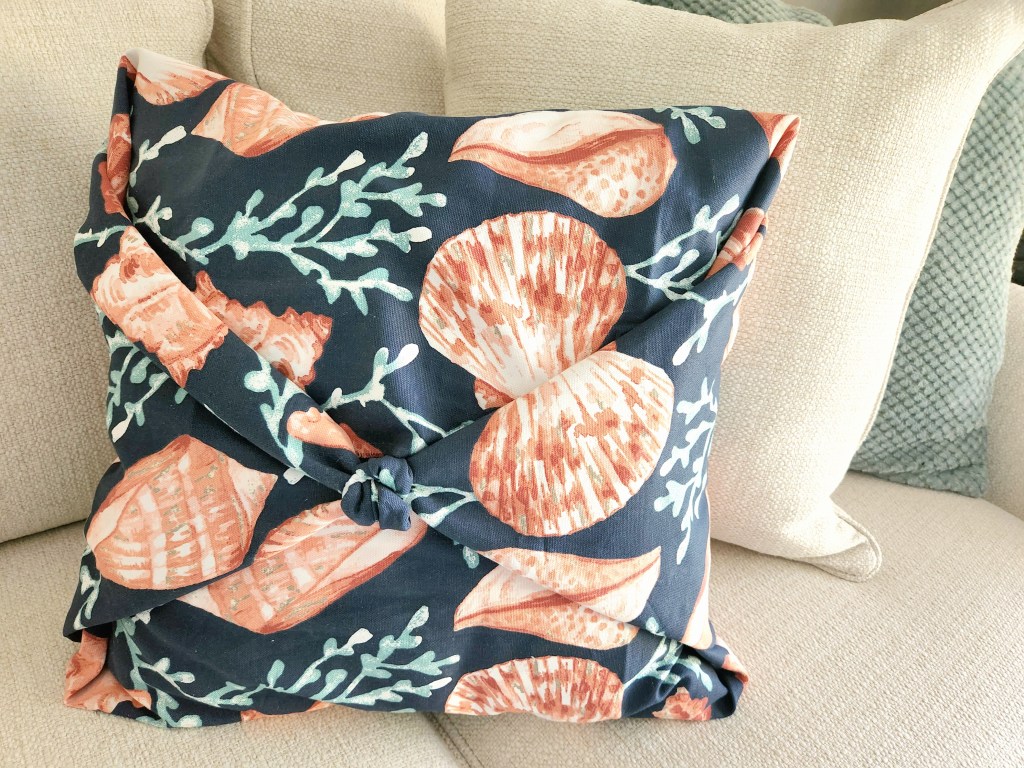 No sew pillowcase covered with shells and corals on a sand-colored sofa along with two other throw pillows.
