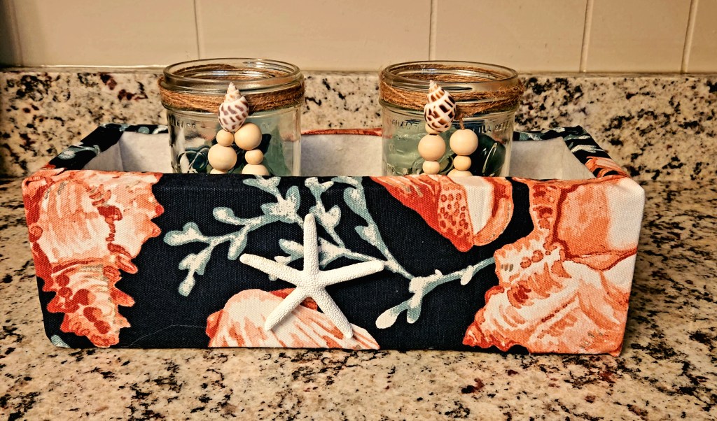 Coastal Centerpiece planter box covered in beachy fabric with mason jars with sea glass rocks inside.