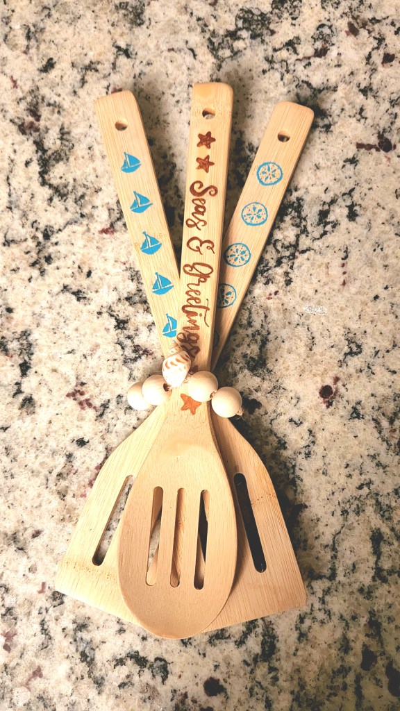 Three wood utensils with the "Seas & Greetings," sailboats, and sand dollars on them.