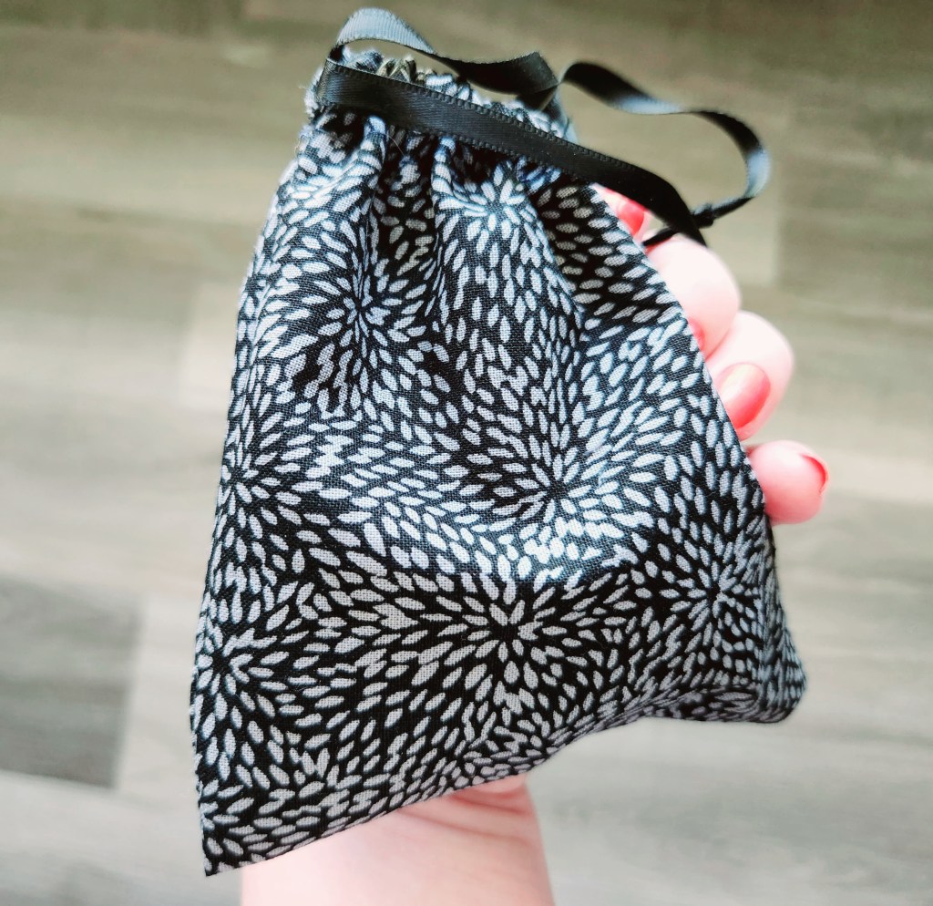 DIY drawstring bag made with black fabric with tiny gray petals and black satin ribbon drawstrings, used as a menstrual disc carrying case.