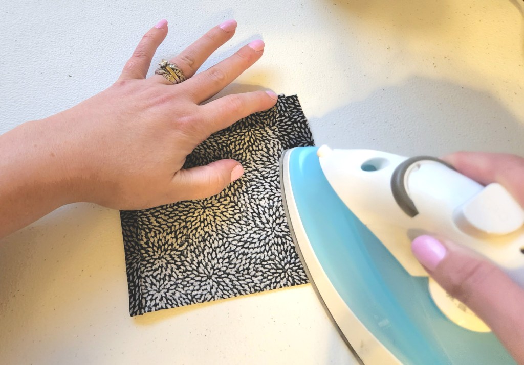 Ironing the 1/2" fabric past the seam on the sides of the drawstring bag down onto the main part of the bag.