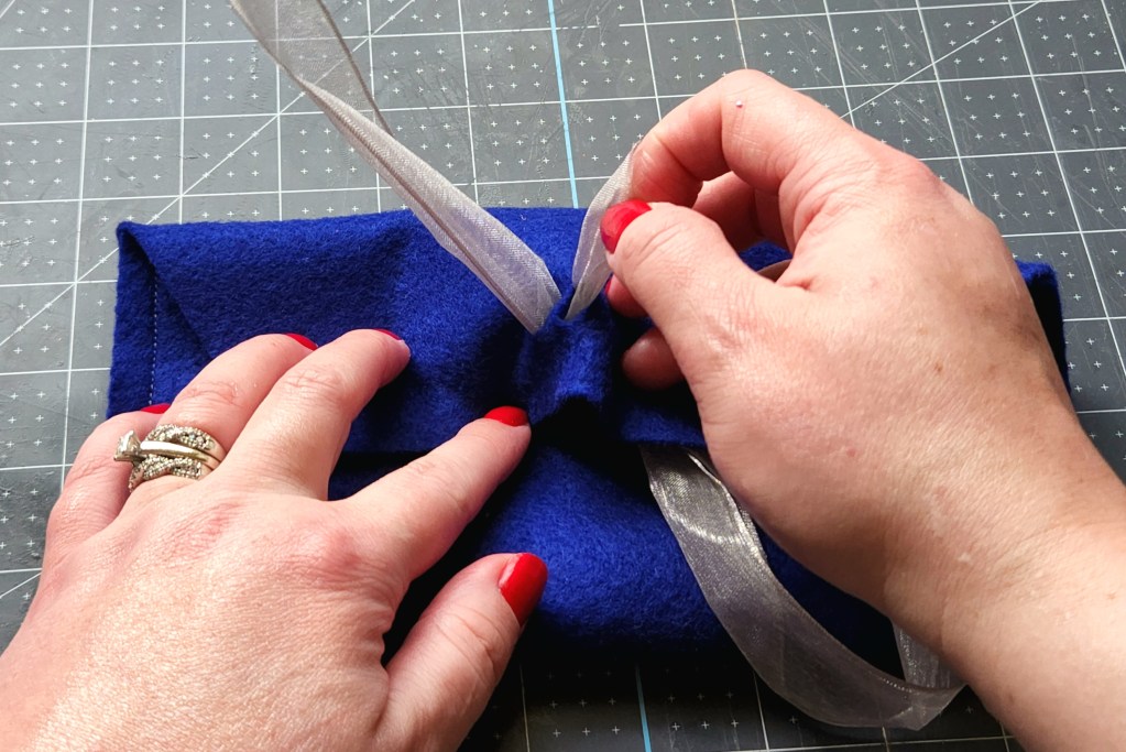 Feeding a 1.5" gray ribbon through the slits in the flap of the felt gift envelope.