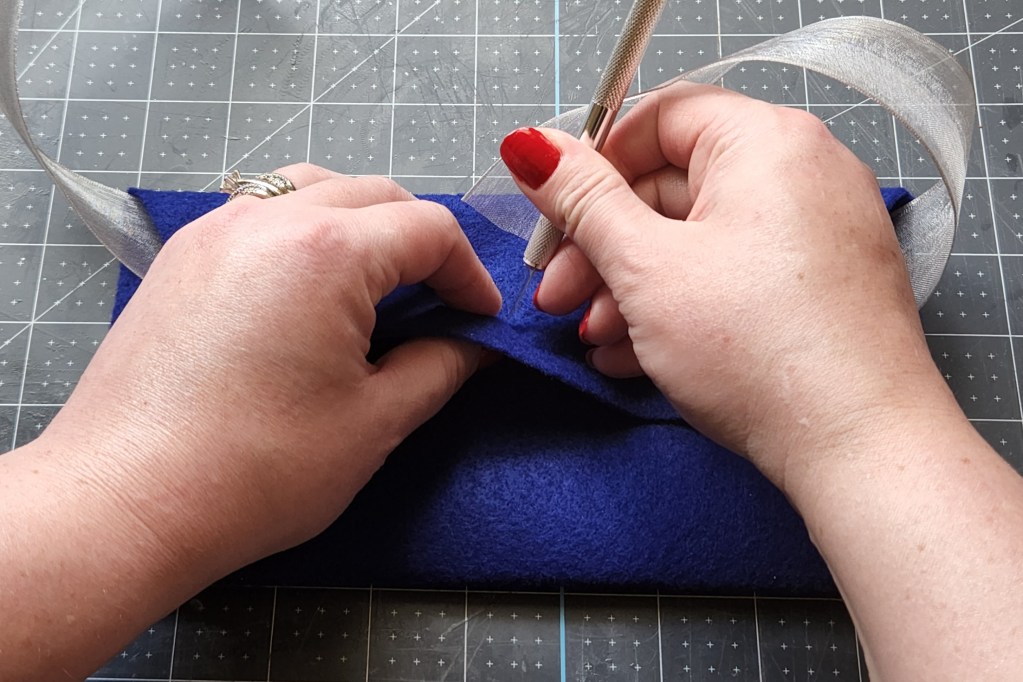Cutting a slit in the flap of the felt envelope to feed the ribbon through.