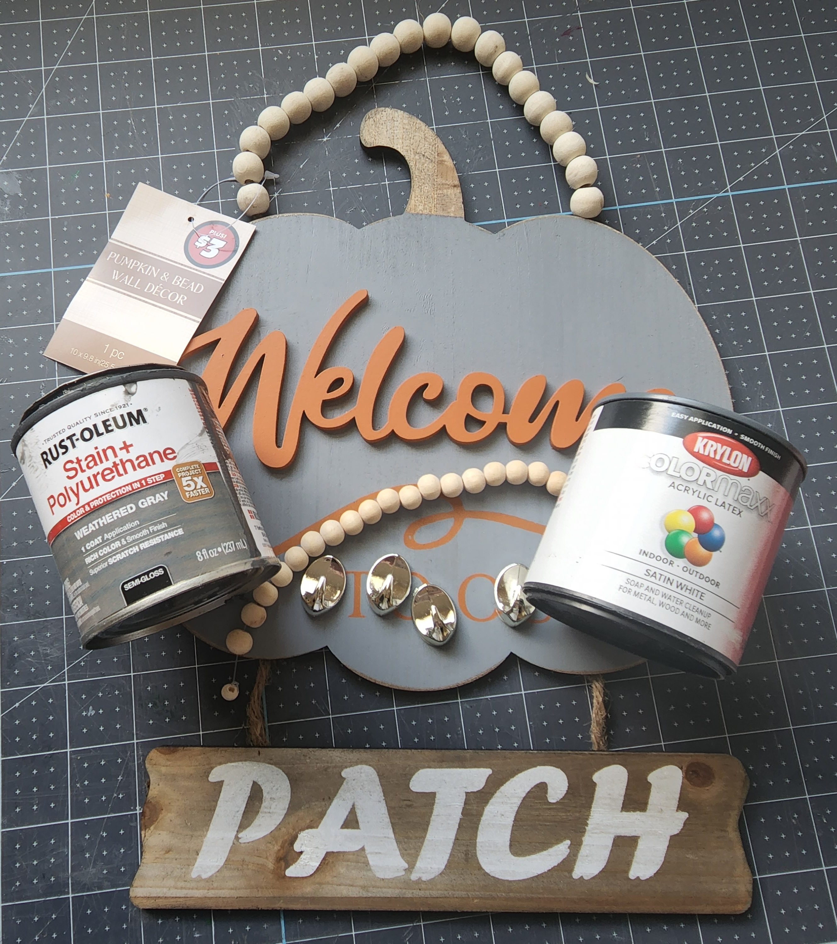 Supplies for the fall pumpkin keyholder: Dollar Tree pumpkin sign with a beaded handle and "welcome to our patch" on it, weathered gray Rust-oleum stain & polyurethane in one, extra wood beads, hooks. and white paint.