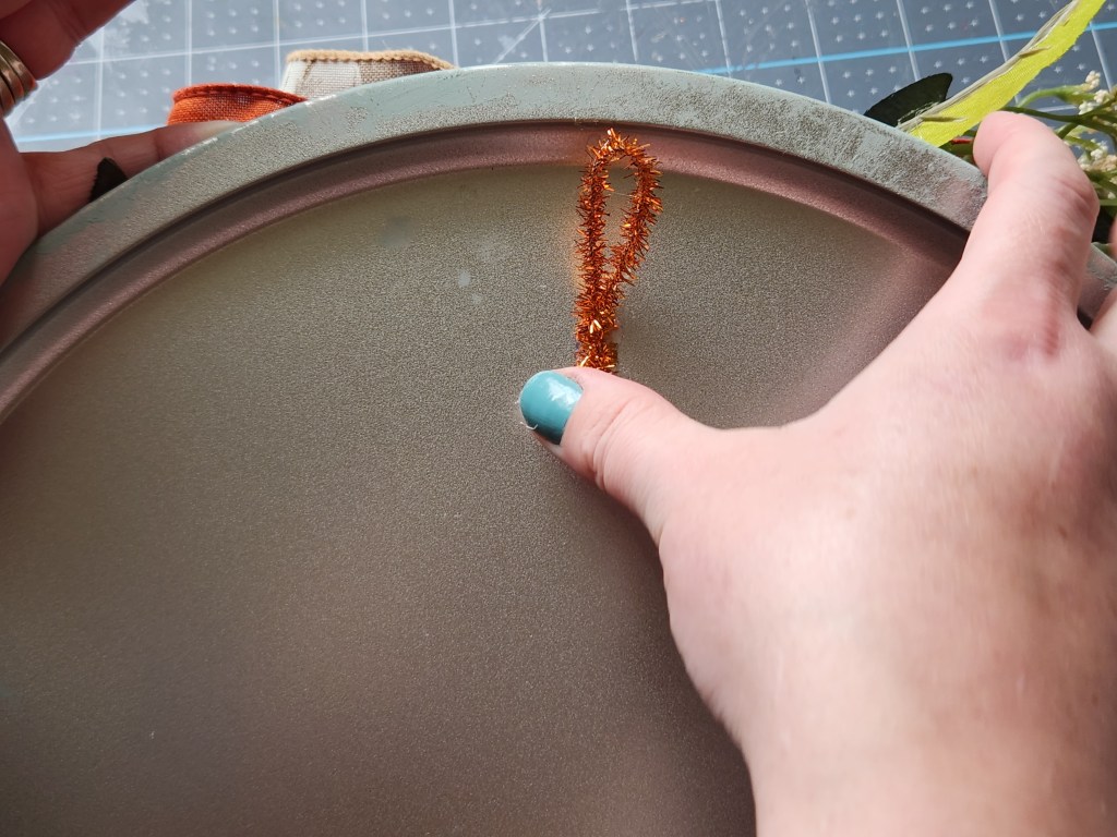 Hot gluing a large loop of pipe cleaner to the back of the pizza pan wreath to hang it on the door.