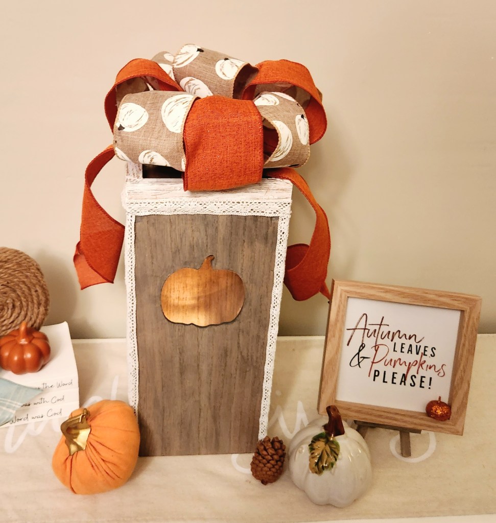 DIY fall lantern with pumpkin cutouts on the sides and an orange ribbon and white pumpkin print bow on top.