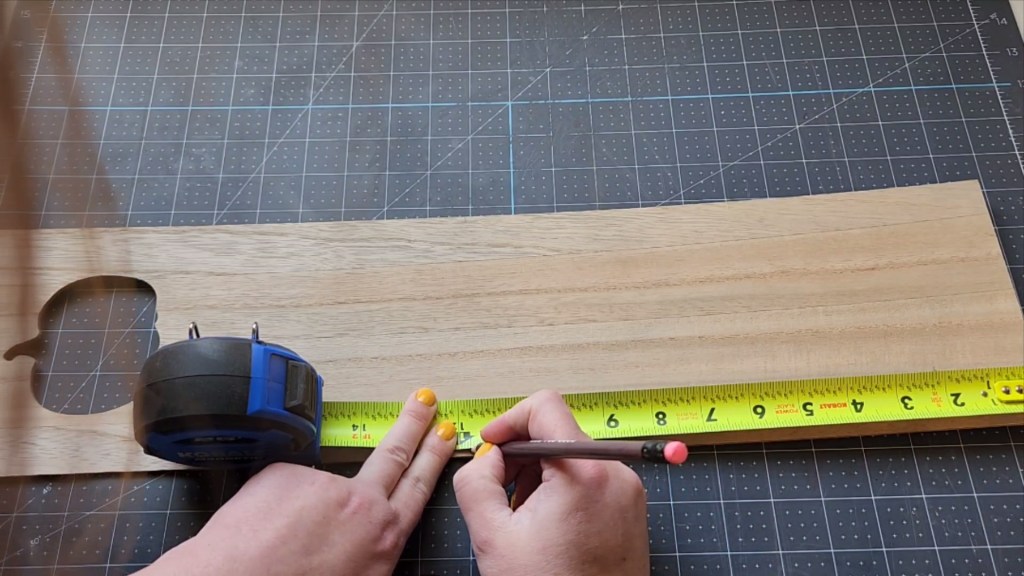 A measuring tape placed at the end of the wood sign and making a pencil mark at 11.75".