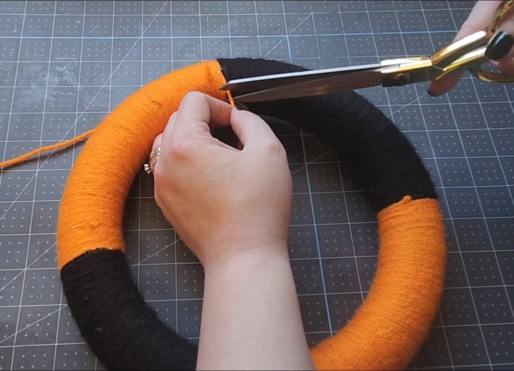 Cutting the end of the orange yarn off the back of the wreath from now covered in black and orange sections of ribbon.