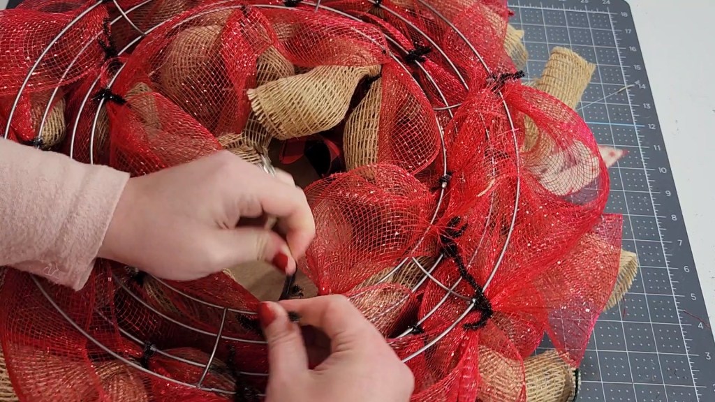 Wrapping pipe cleaners attached to the joy sign around the deco mesh wreath form.