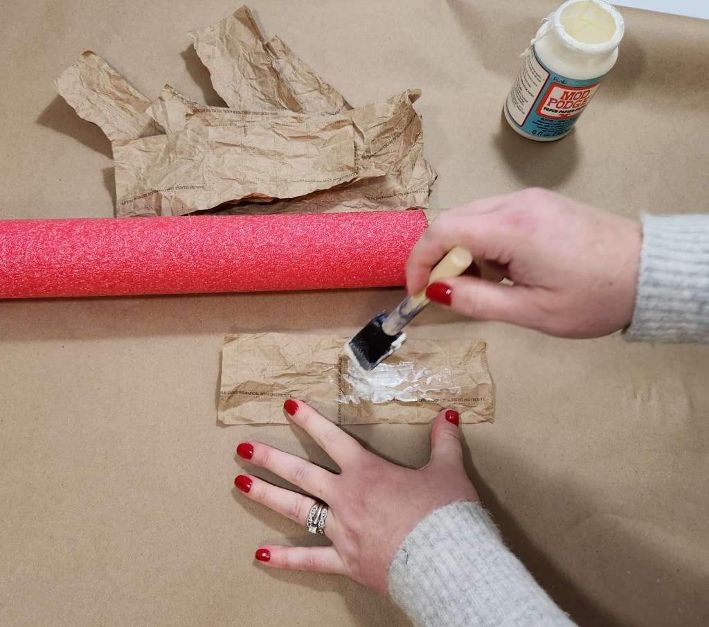 Brushing Mod Podge on the back of a strip of kraft paper.