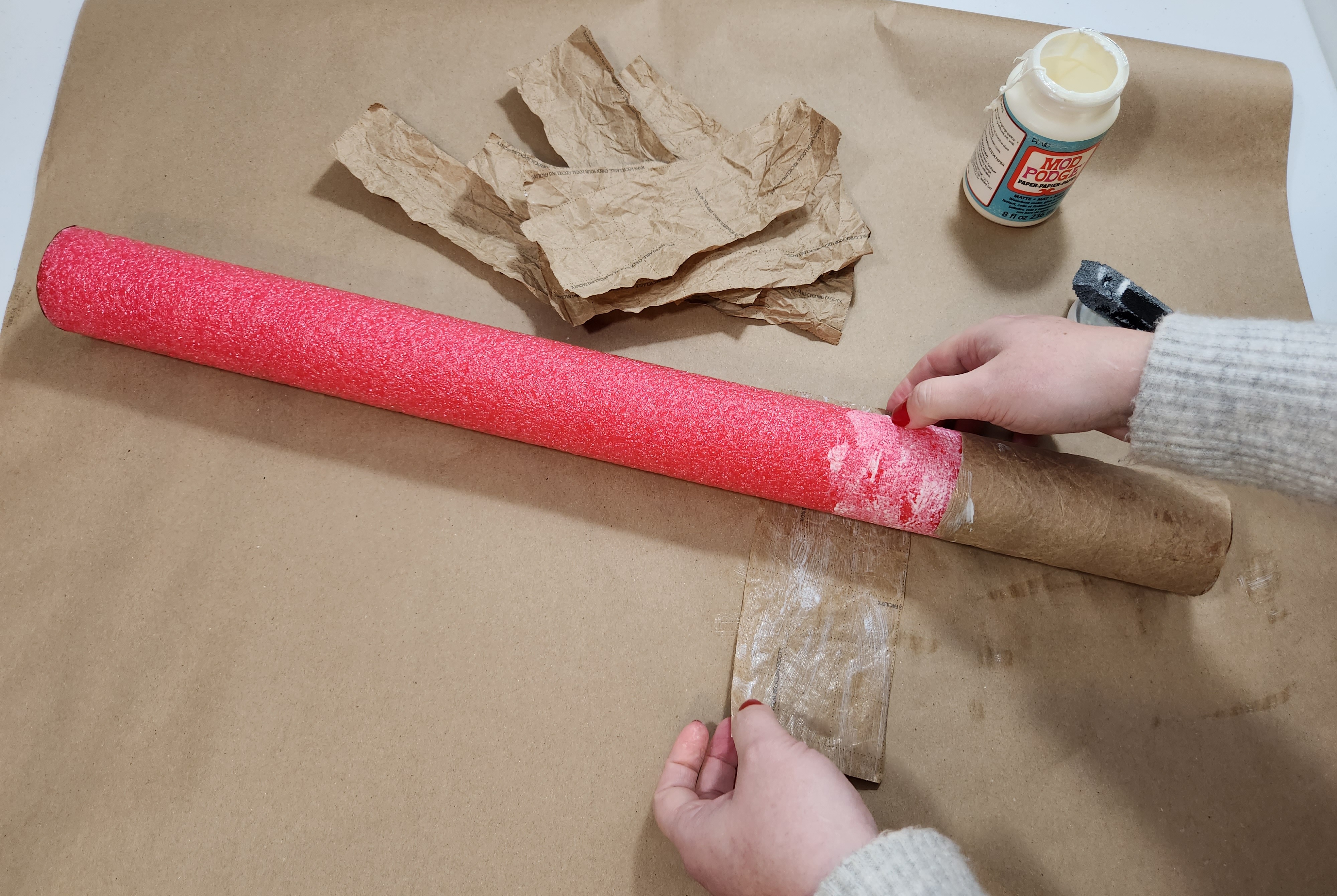 Wrapping a piece of kraft paper around a pool noodle covered with Mod Podge to create the look of a faux birch log.