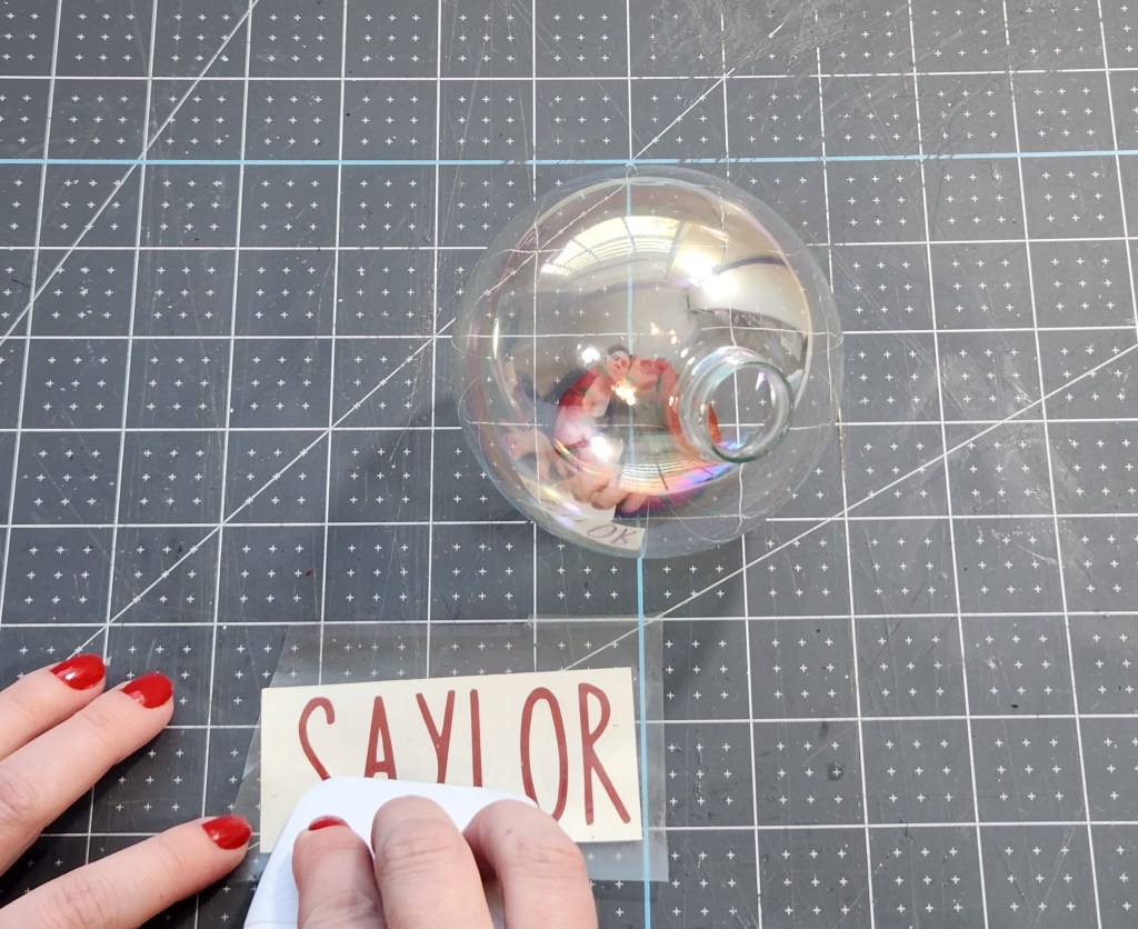 Using contact paper to remove the vinyl from the backing to transfer it onto the ornament glass.