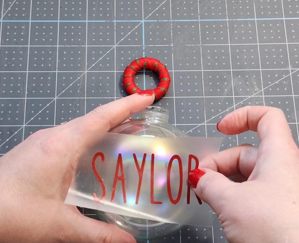 Using contact paper to place the vinyl name "Saylor" onto the ornament glass.
