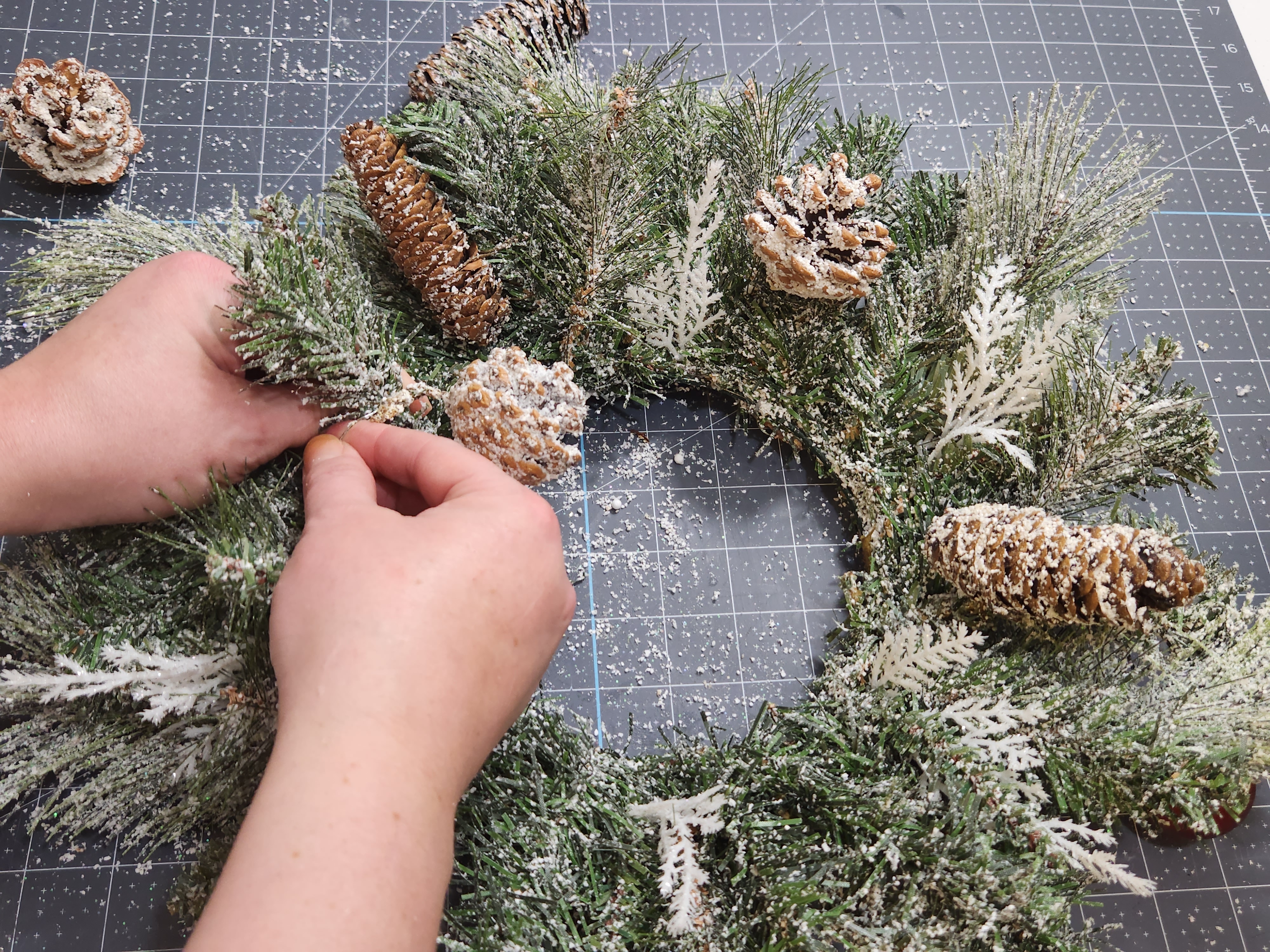 Wrapping a pinecone around the wreath with floral wire.