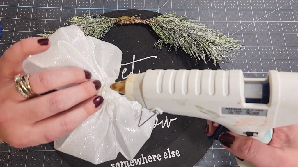 Squeezing hot glue on the back of a white glittery four loop bow.