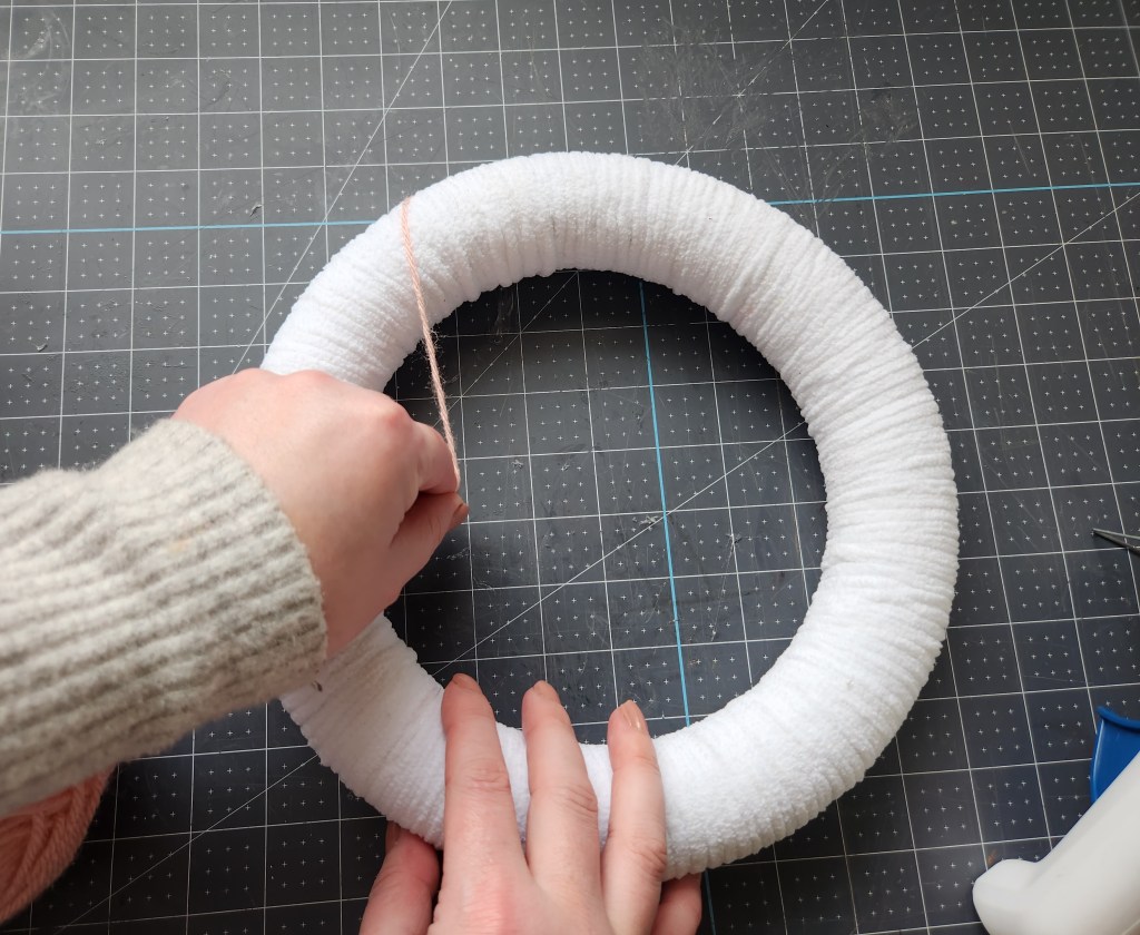 Wrapping pink yarn around the front of the chenille yarn wrapped wreath in a diagonal pattern.