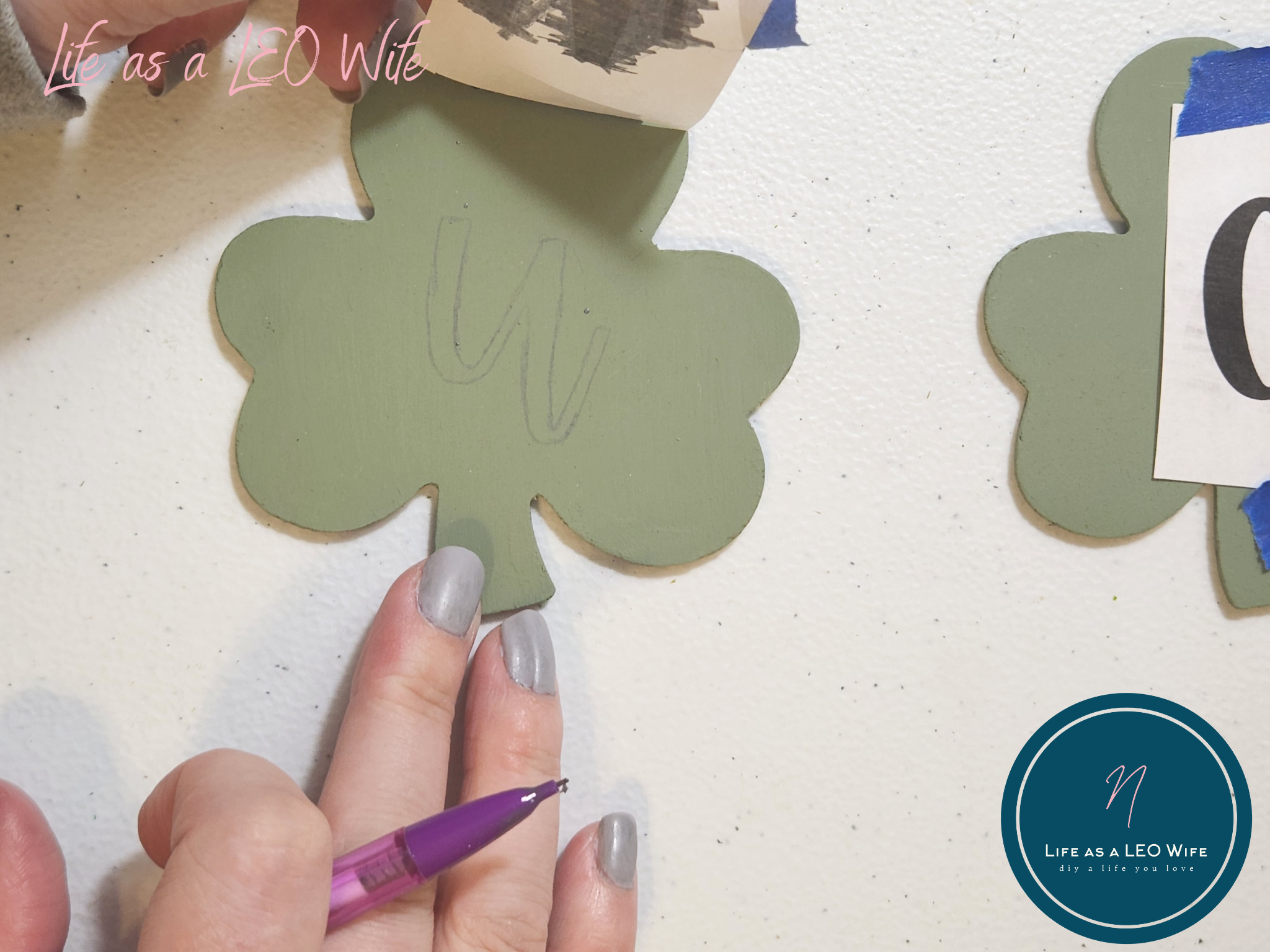 Lifting the paper with the letter "u" up from the shamrock ensuring that the pencil outline of the letter is on it.