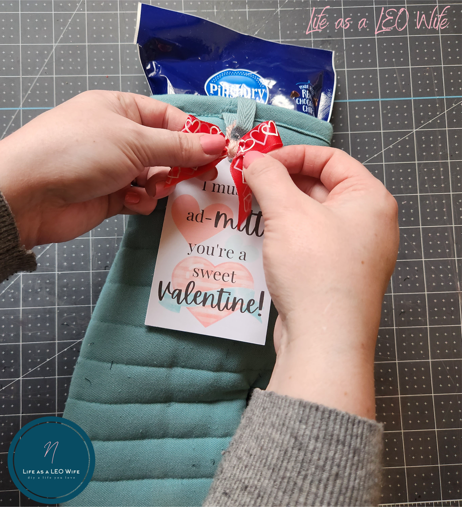 Placing the red bow with hot glue onto the Valentine's teachers gift tag.