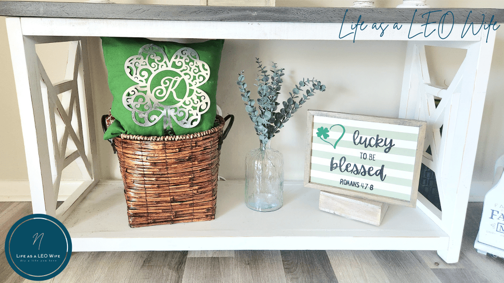 St. Patrick's Day shamrock monogrammed pillow sitting in a basket on a console table sitting next to greenery in a vase jar and a "lucky to be blessed" sign.