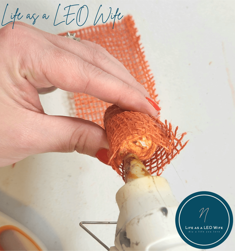 Squeezing hot glue to the top of a faux carrot to attach the burlap to the top.