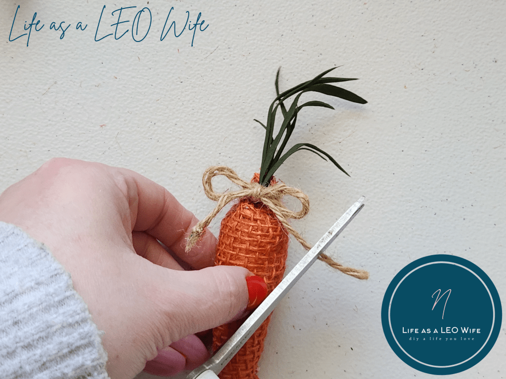 Cutting excess twine from the bow around the top of a faux carrot to use to attach to it the spring garland.
