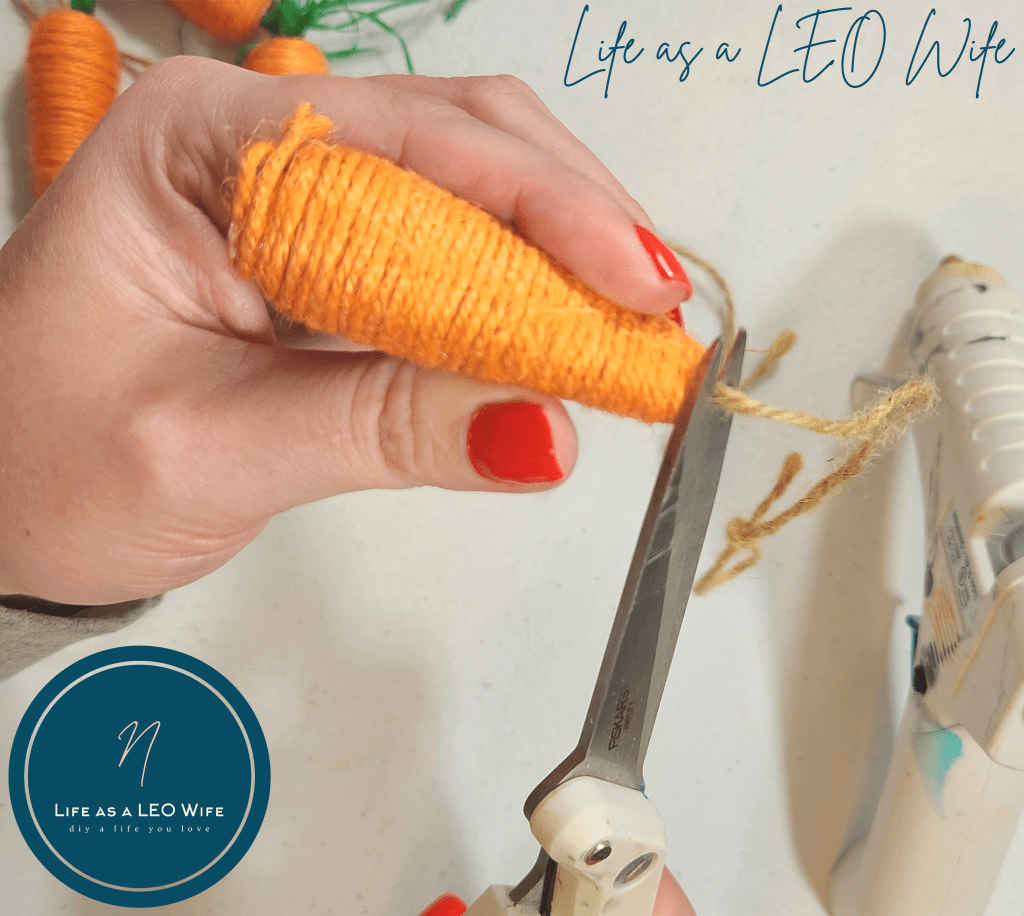 Cutting twine from the bottom of a faux carrot that had held it on the Dollar Tree spring carrot garland.