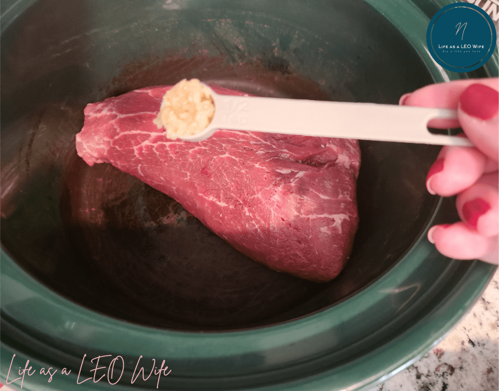 Adding minced garlic to a Crockpot with a rump roast in it.