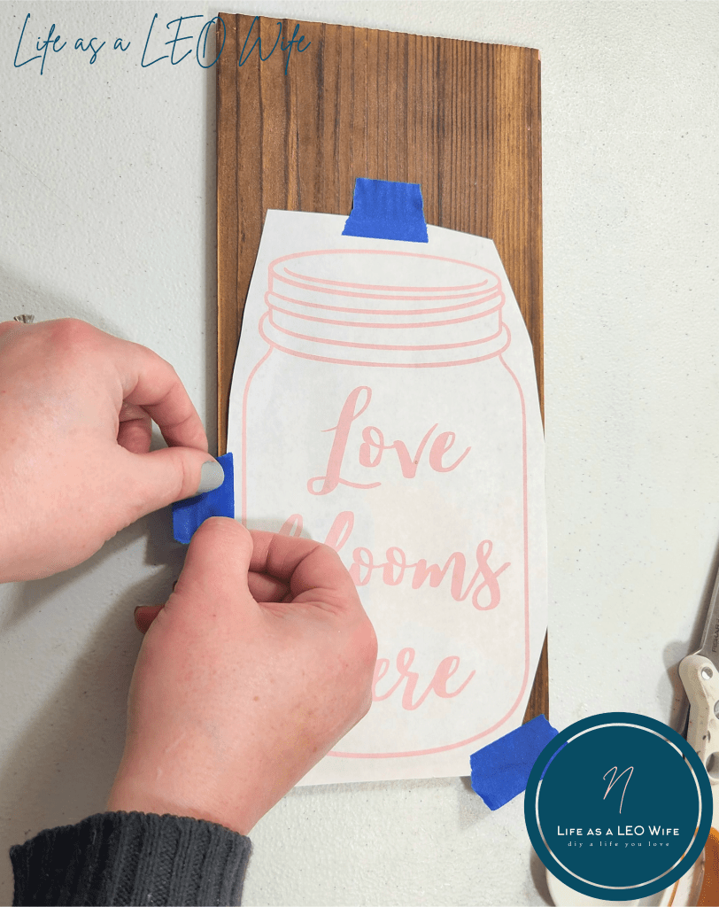 Taping mason jar design on a wood sign to give as a Mother's Day gift.