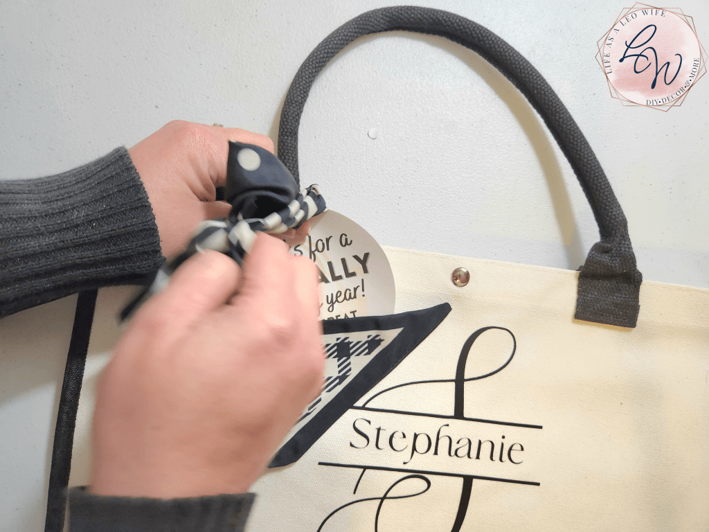 Tying a bow in the scarf which is attaching the end of the year teacher gift tag to the beach tote gift.