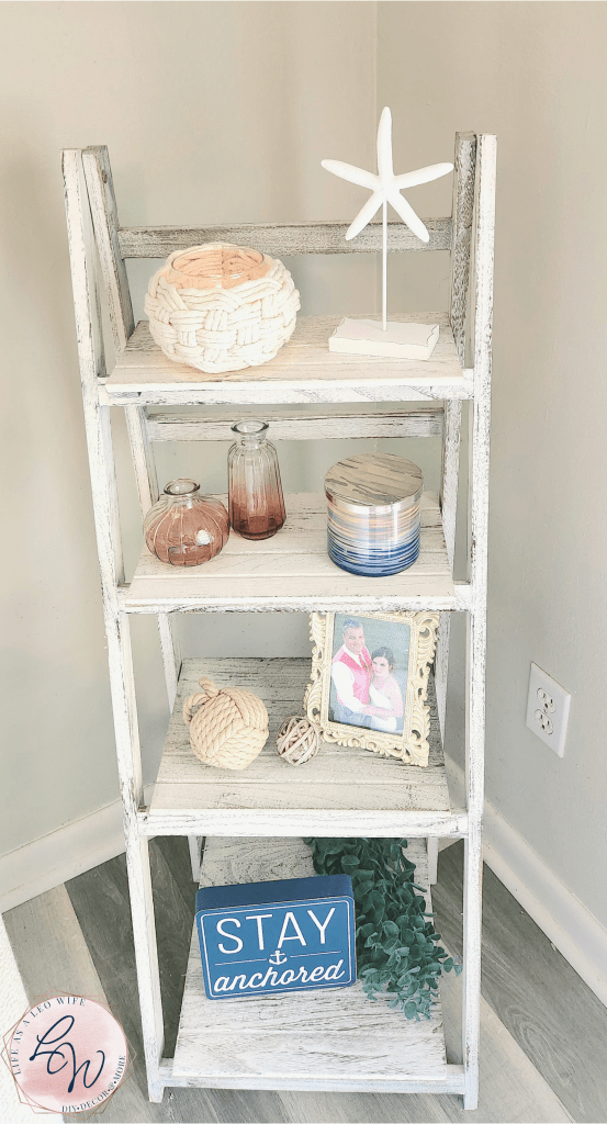 A white farmhouse style ladder shelf with a DIY knotted rope vase on the top shelf and other decorative pieces on the other 3 shelves.