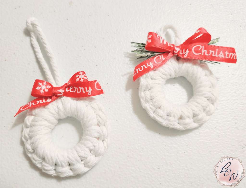 Two finished mini wreath ornaments made with white macrame cord, one topped with a red bow with "Merry Christmas" on it and the 2nd topped with the bow & Christmas greenery.