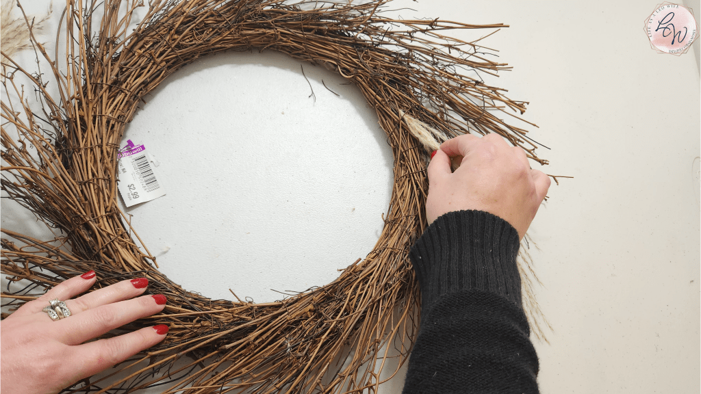 Adding the 1st piece of dried grass to a fall twig wreath form.