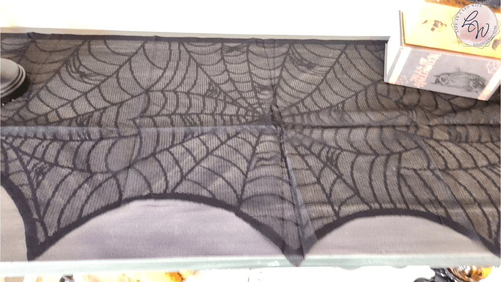 Black spiderweb mantle scarf on the center of the sofa table which serves as the faux mantle for Halloween.